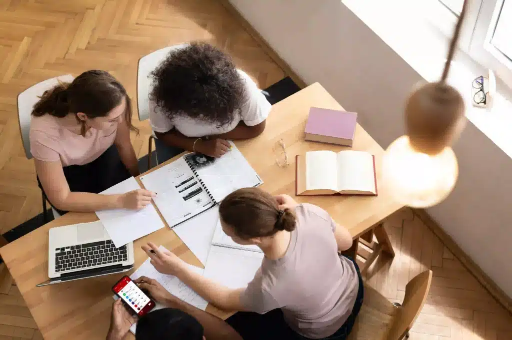 Groupe d’étudiants travaillant ensemble autour d’une table avec des livres et un ordinateur portable.